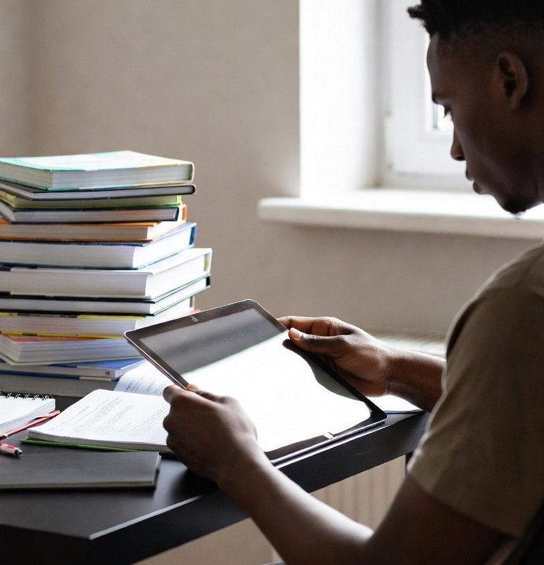student reading a tablet surrounded by a pile of unused textbooks